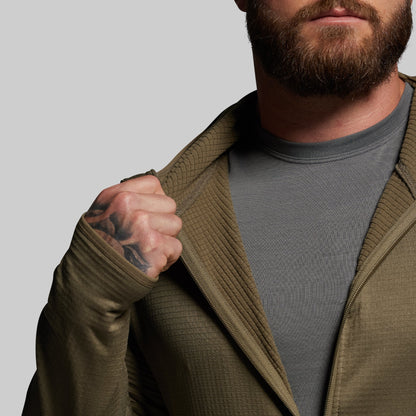 Man wearing a green zip up over a gray shirt against a plain background