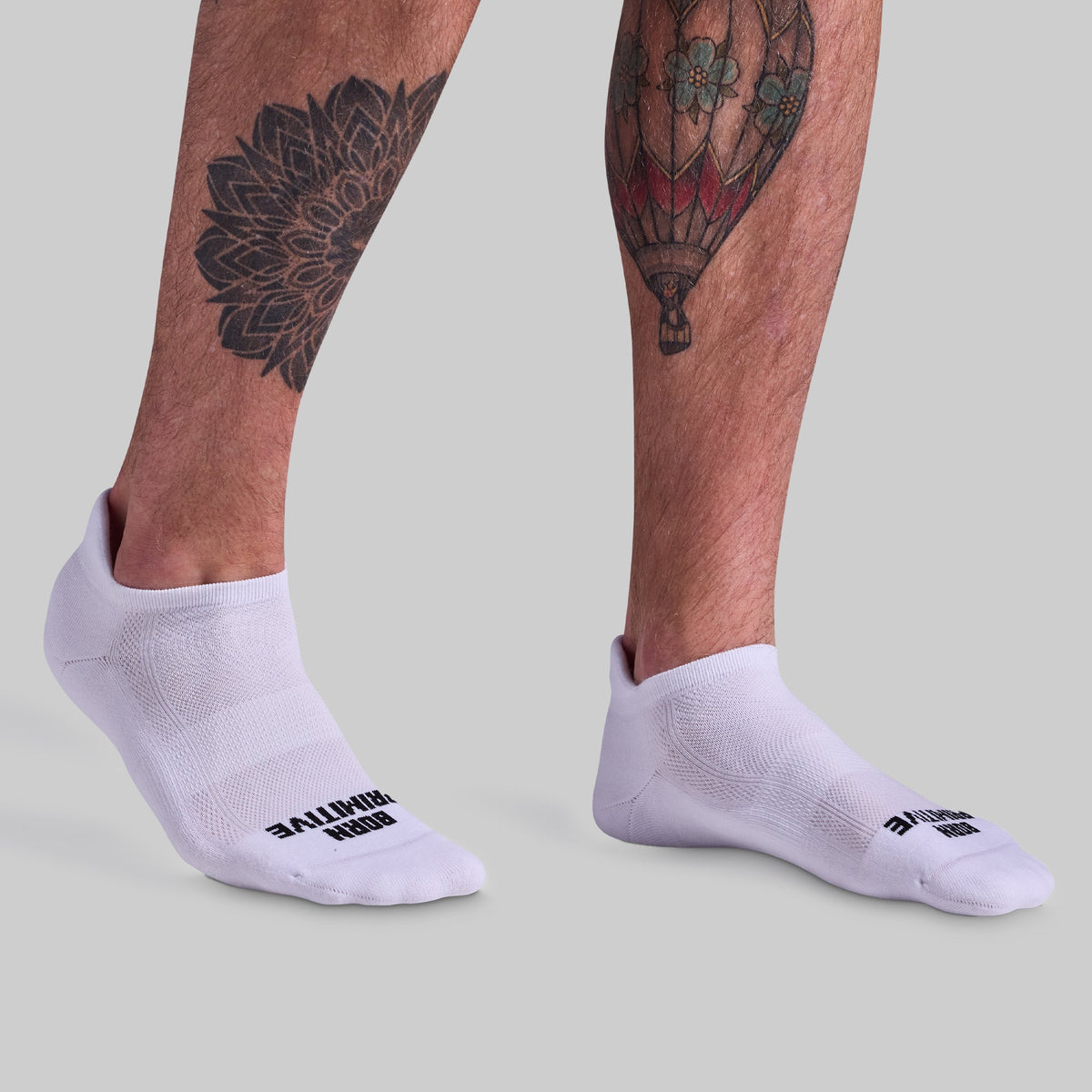 White socks with brand logo worn by a person with tattoos on a light gray background