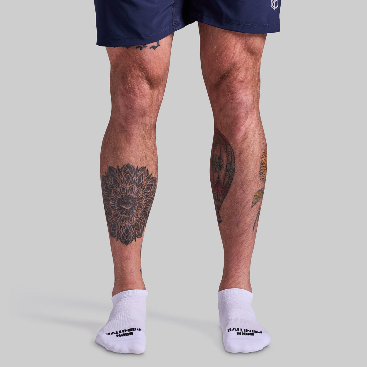Person wearing navy shorts and white socks with visible tattoos on legs against a gray background
