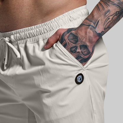 Person wearing tan shorts with a brand logo, showing a tattooed arm.