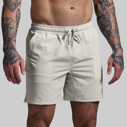 Beige shorts worn by a person with tattoos on a plain background