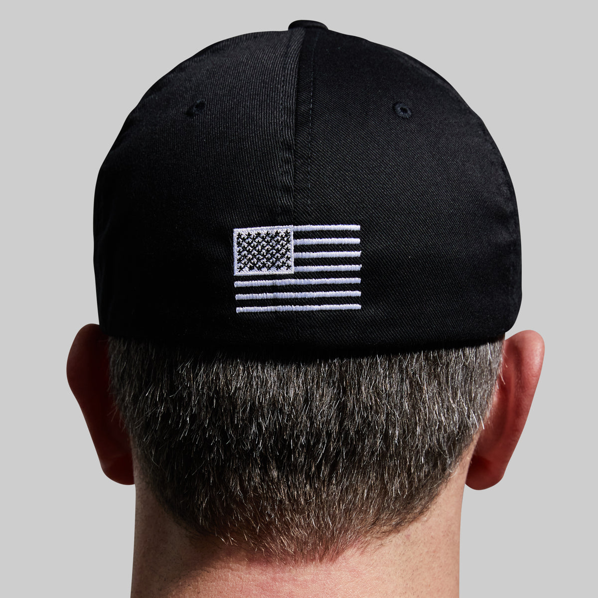 Black cap with American flag patch worn by a person on a gray background