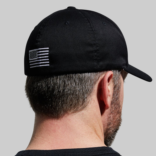 Black cap with American flag patch worn by a person on a gray background