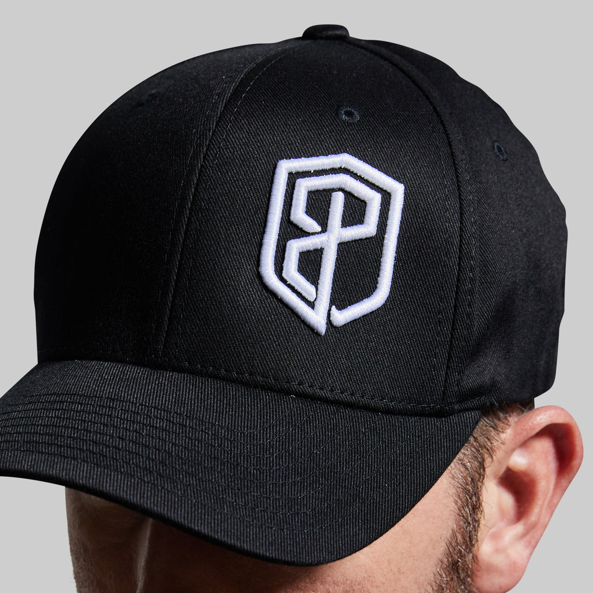 Black cap with a white logo worn by a person on a gray background