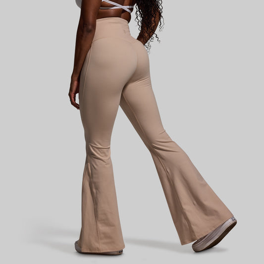Beige flared pants worn by a person on a gray background
