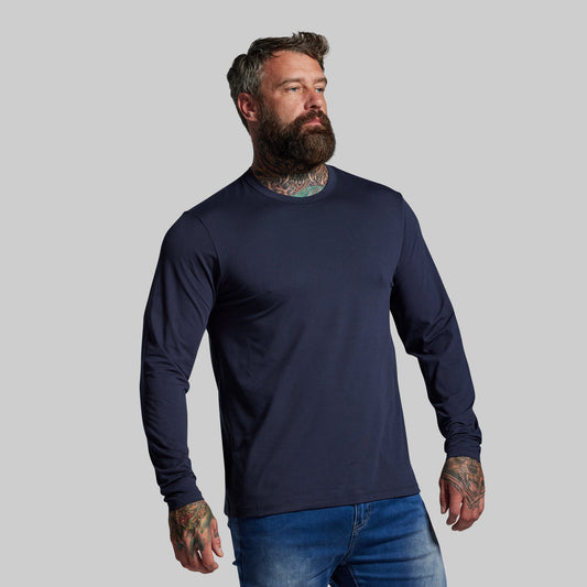 Man wearing a navy long-sleeve shirt and blue jeans against a gray background