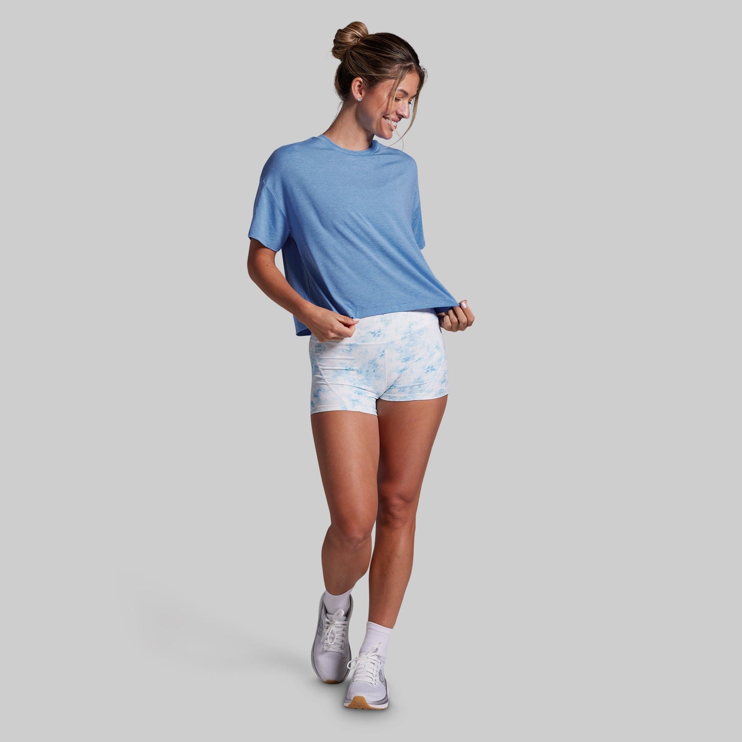 A woman modeling a light blue short-sleeve t-shirt and light blue/white patterned athletic shorts against a solid gray background.