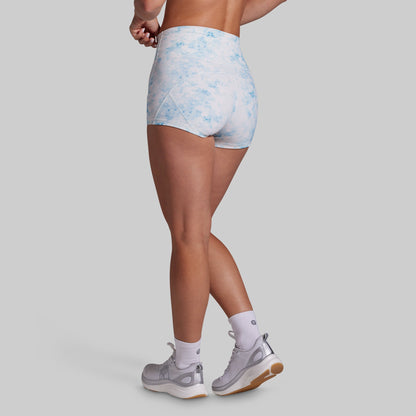 Rear three-quarter view of a model wearing high-waisted athletic shorts with a light blue and white watercolor pattern, paired with white socks and gray running shoes, against a solid gray background.