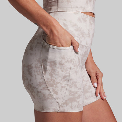 Close-up of a model wearing high-waisted athletic shorts with a beige and off-white mottled pattern, featuring a side pocket and a matching sports bra partially visible.