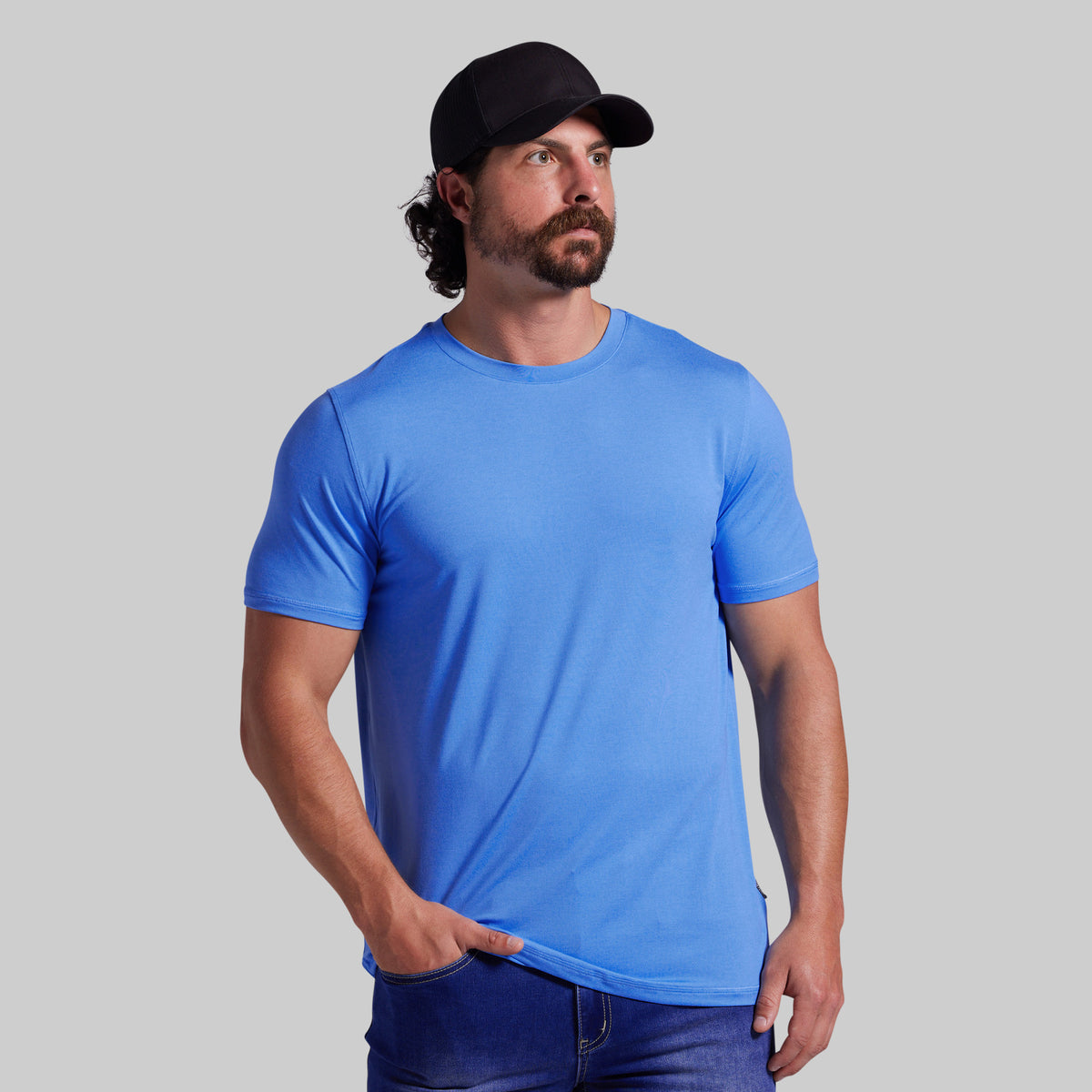 A man wearing a bright blue short-sleeve crewneck t-shirt and a black baseball cap, standing against a solid gray background.