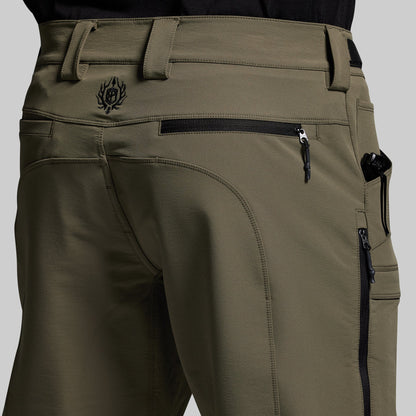 Close-up of olive green outdoor pants with zippers and a logo on a gray background