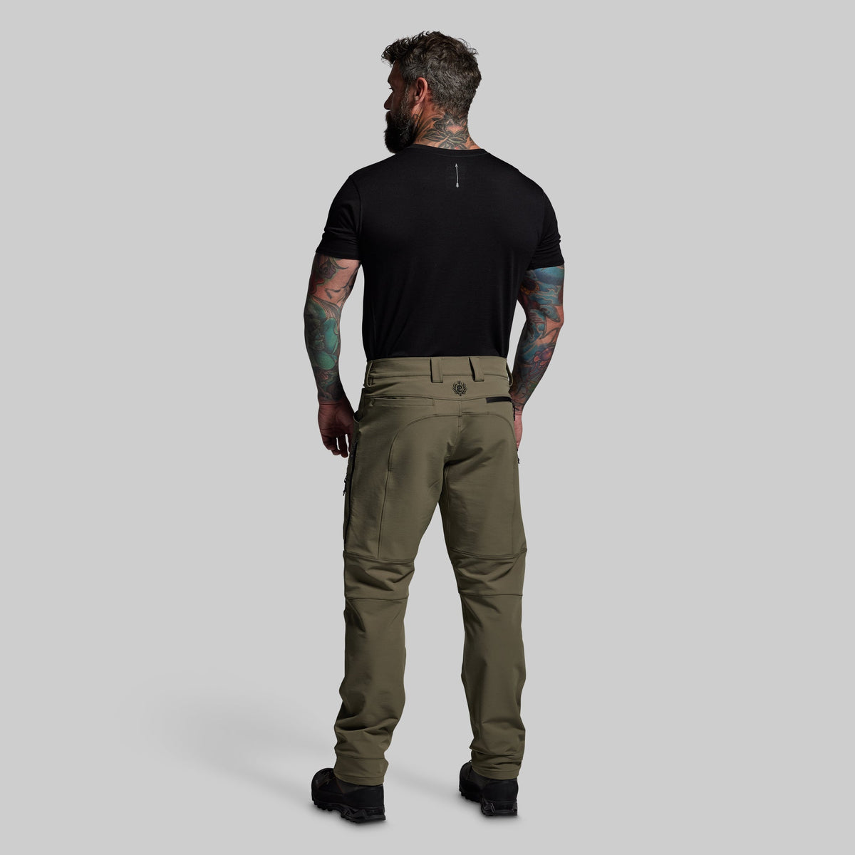 Man wearing olive green pants and a black t-shirt on a gray background