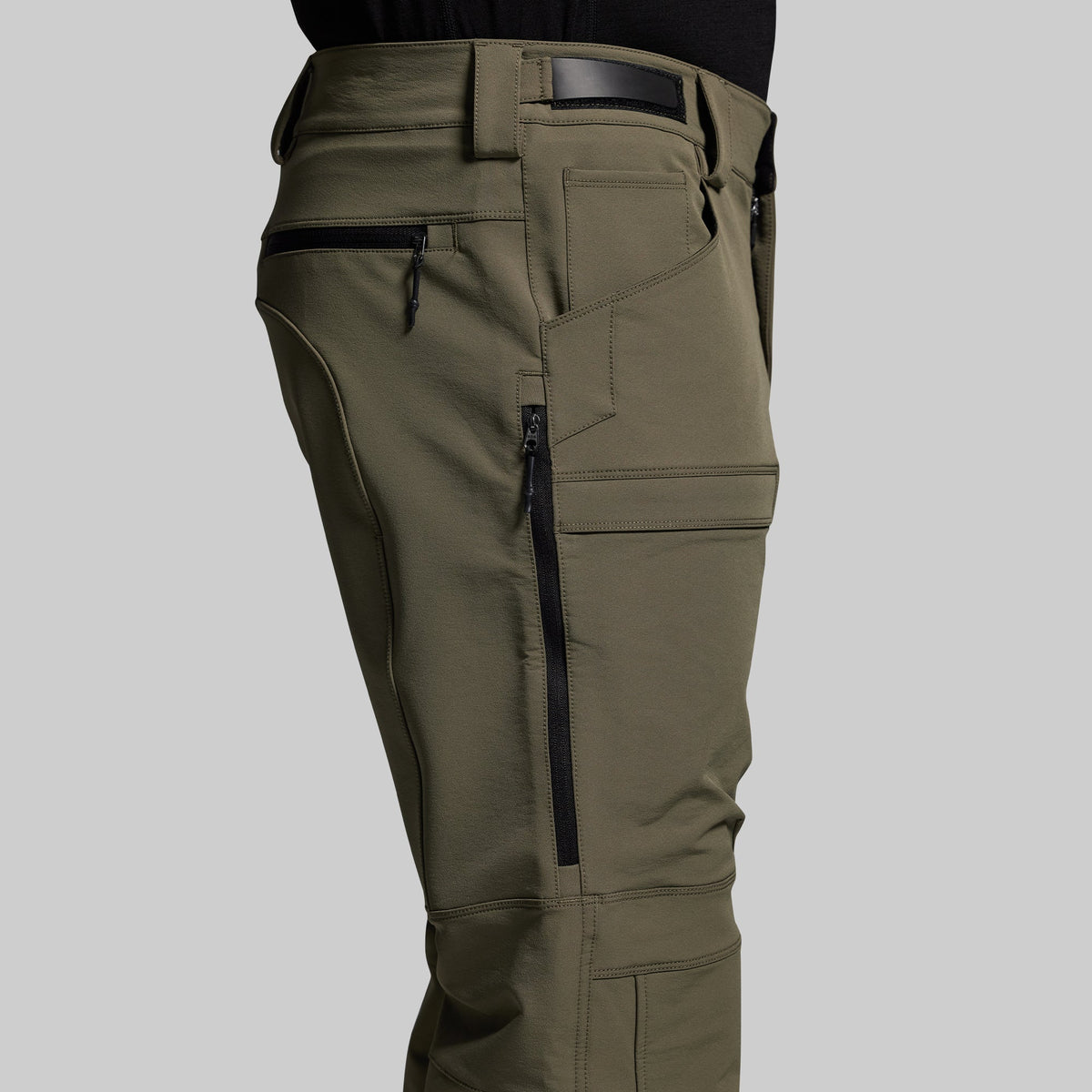 Olive green outdoor pants with zippered pockets on a gray background