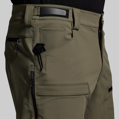 Close-up of olive green outdoor pants with multiple pockets and zippers on a gray background