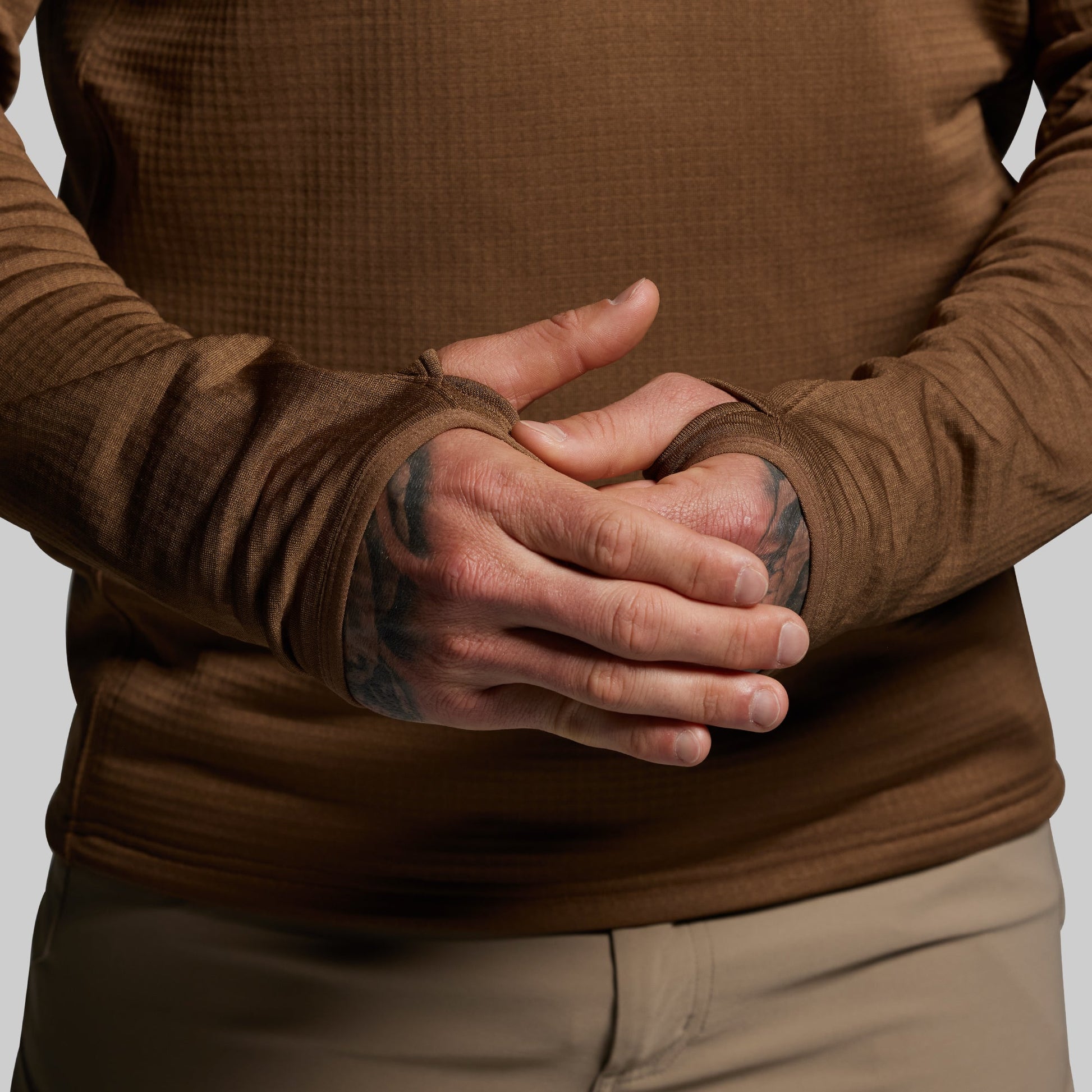 Person wearing a brown long-sleeve shirt with thumbholes on a plain background