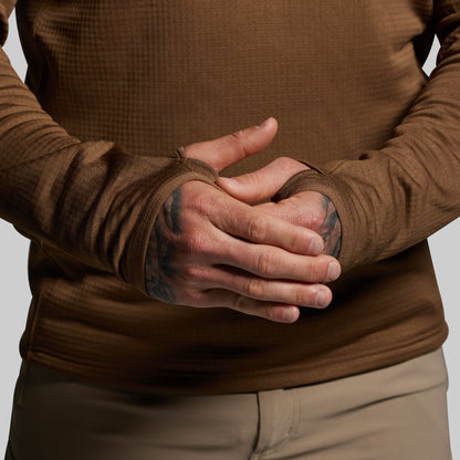 Person wearing a brown long-sleeve shirt with thumbholes on a plain background