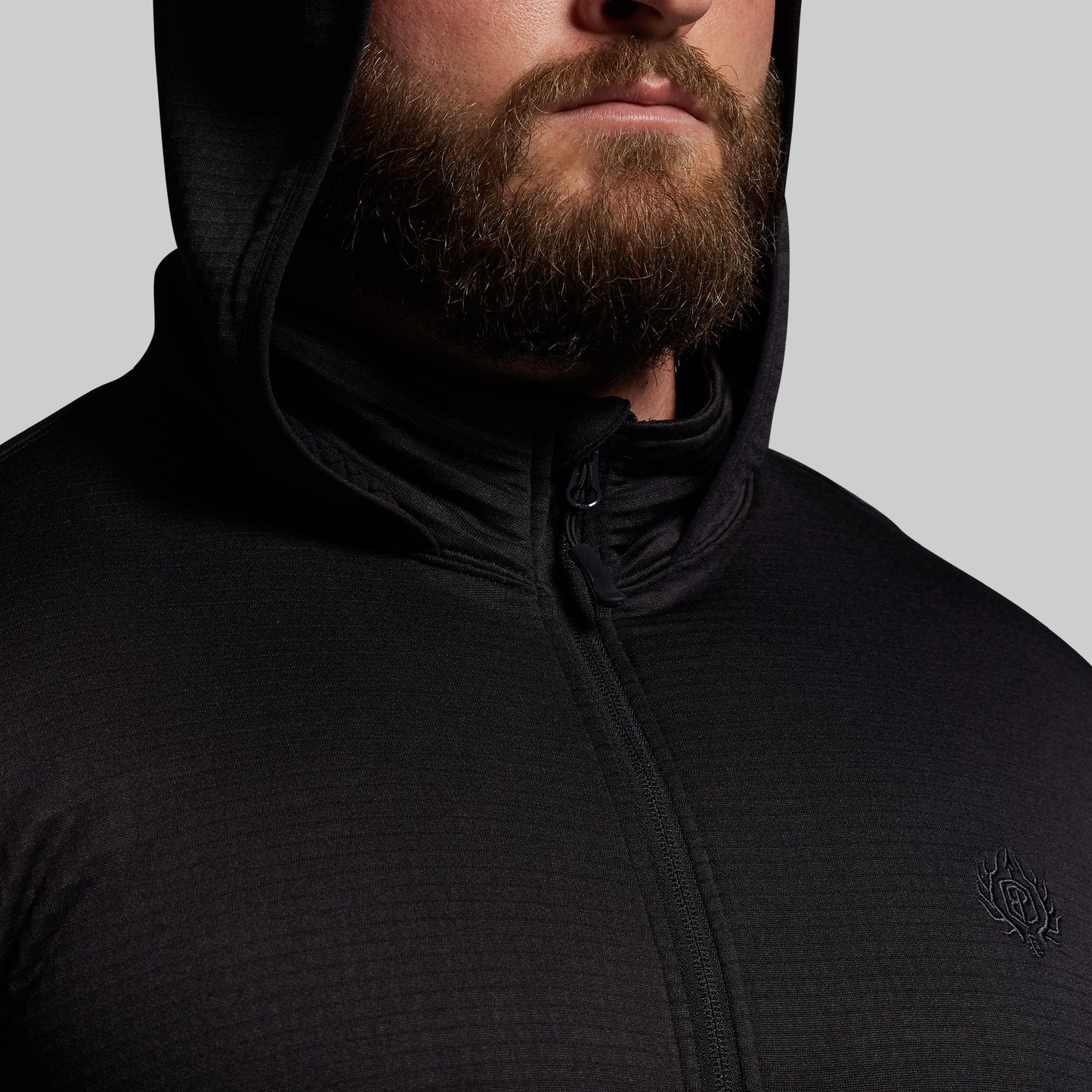Person wearing a black hoodie with a brand logo on a gray background