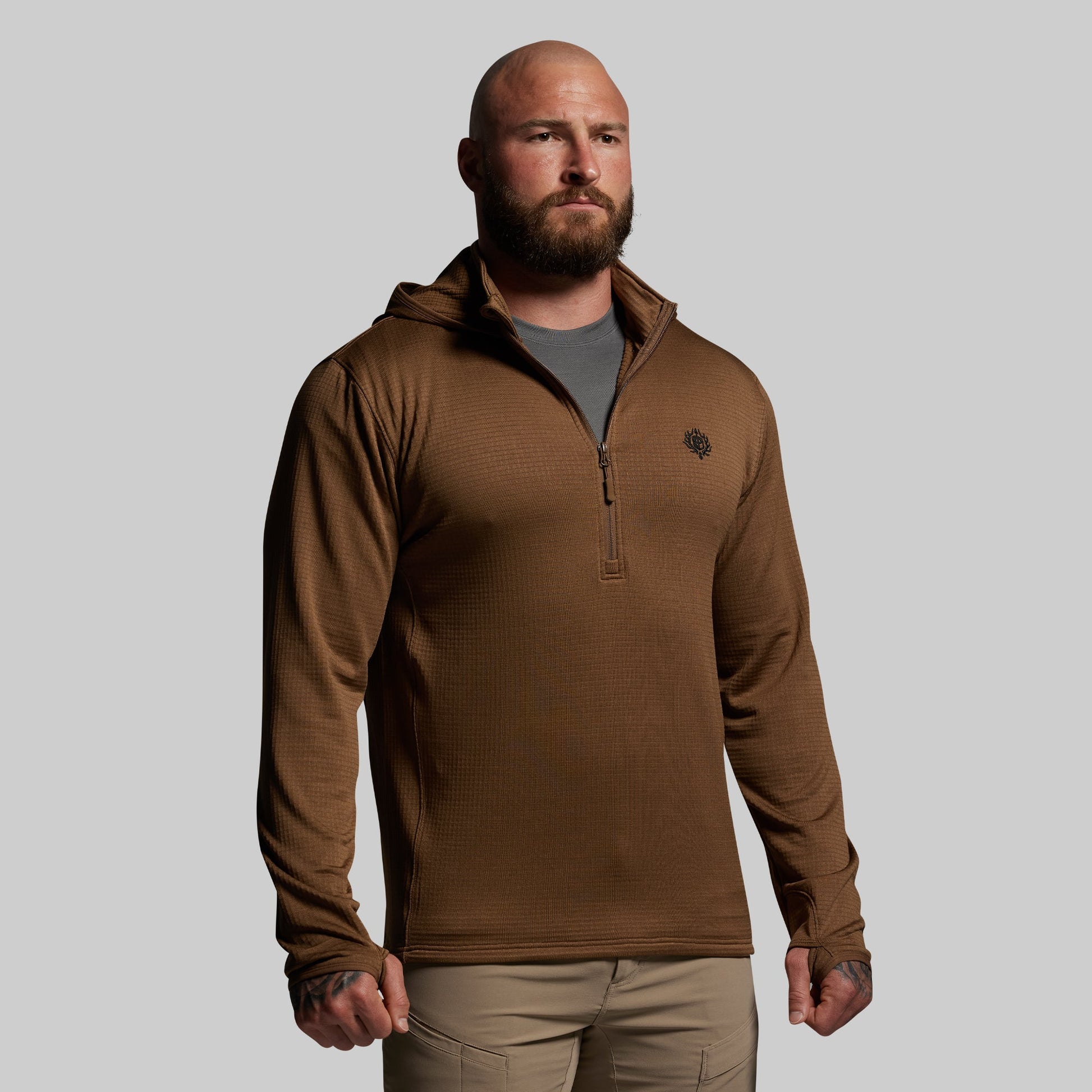 Man wearing a brown pullover with a small logo on a gray background