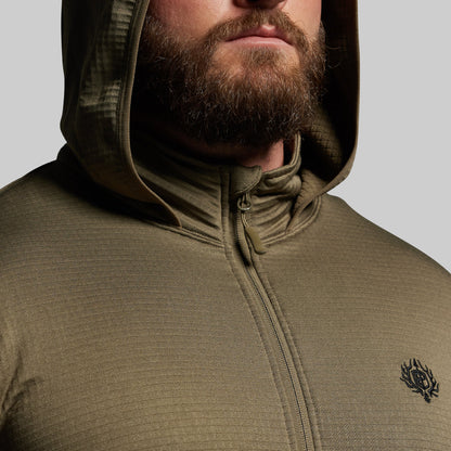 Person wearing a green hooded mid layer with a brand logo on a gray background