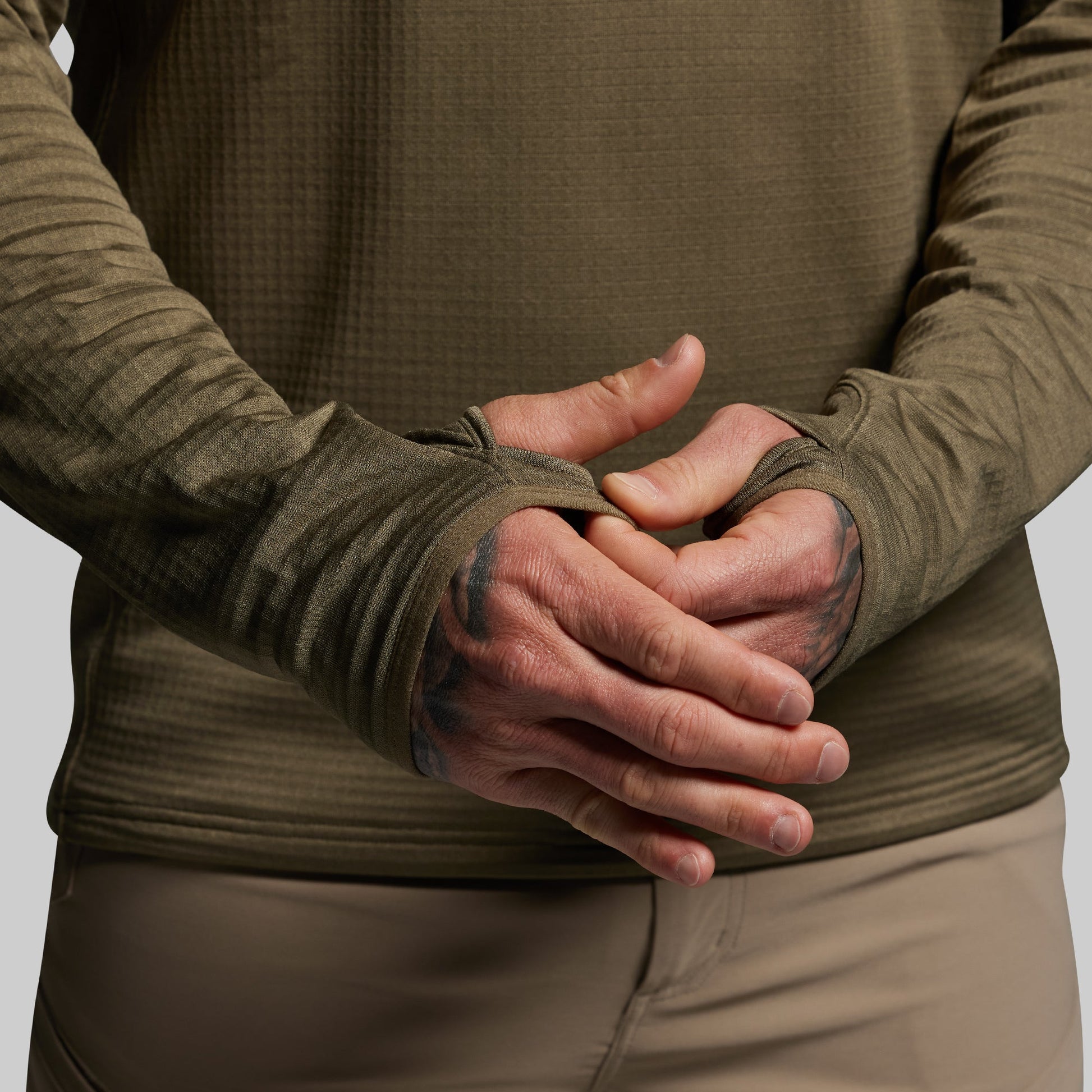 Person wearing a green long-sleeve shirt focusing on thumbholes.