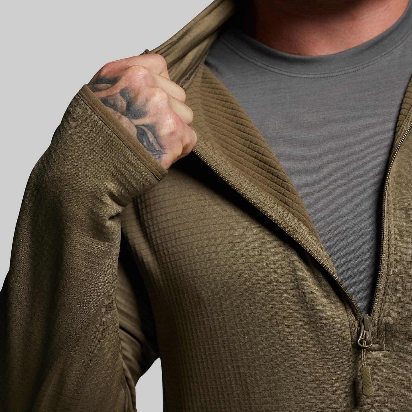 Person wearing a green quarter zip hoodie with a gray shirt underneath, on a plain background