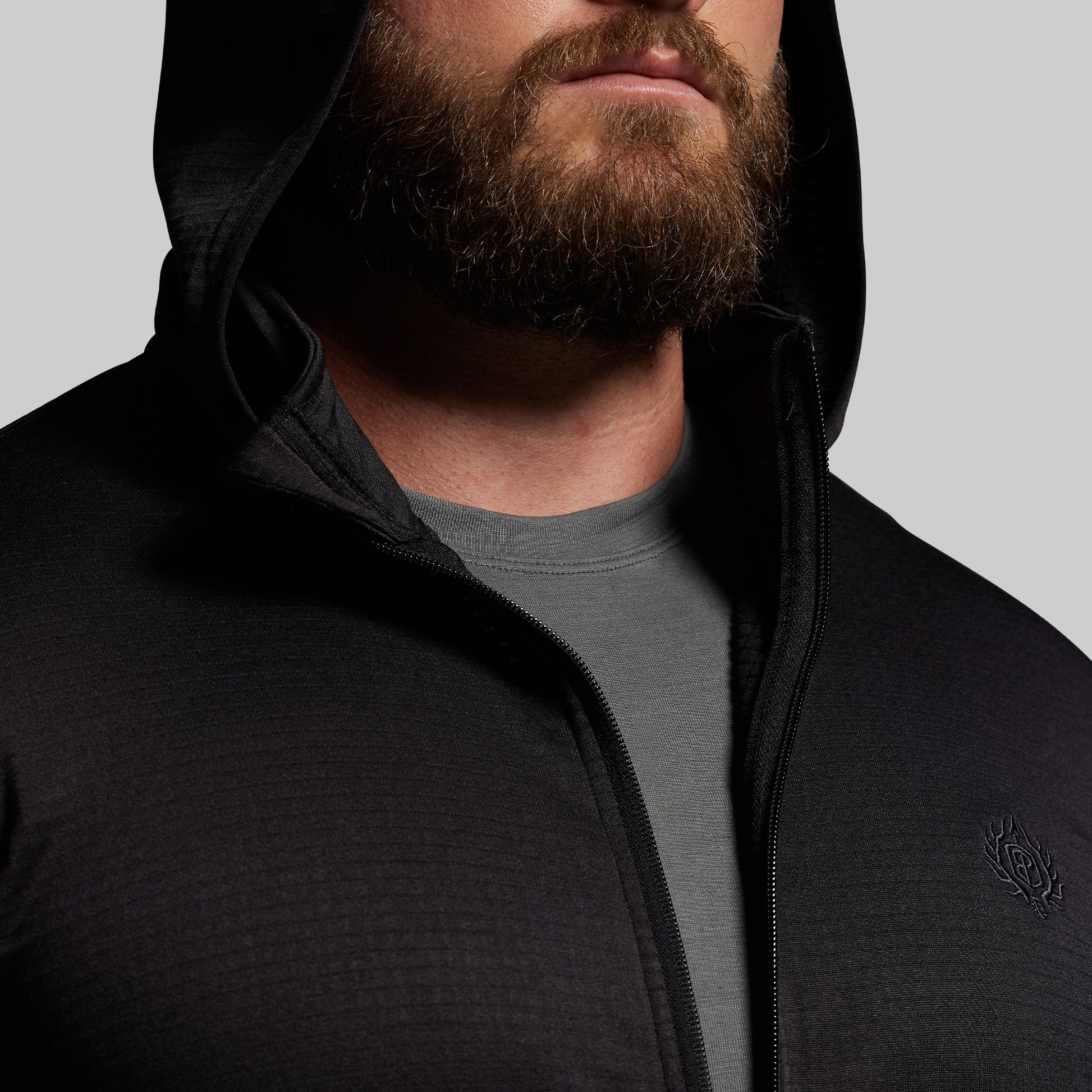 Man wearing a black hoodie with a brand logo on a gray background