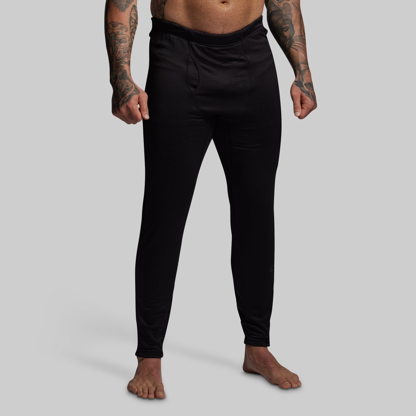 Person wearing black base layer pants on a gray background