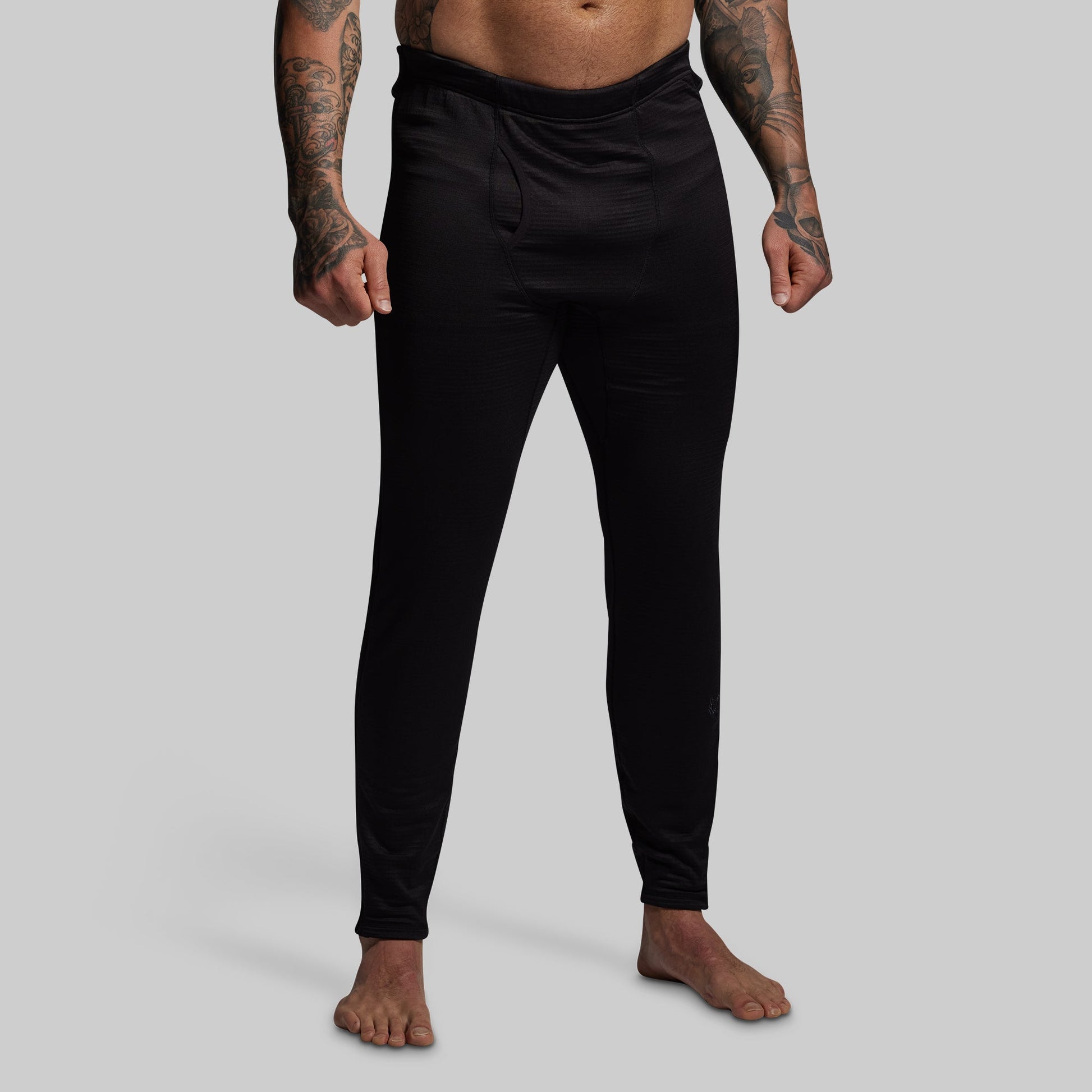 Person wearing black base layer pants on a gray background