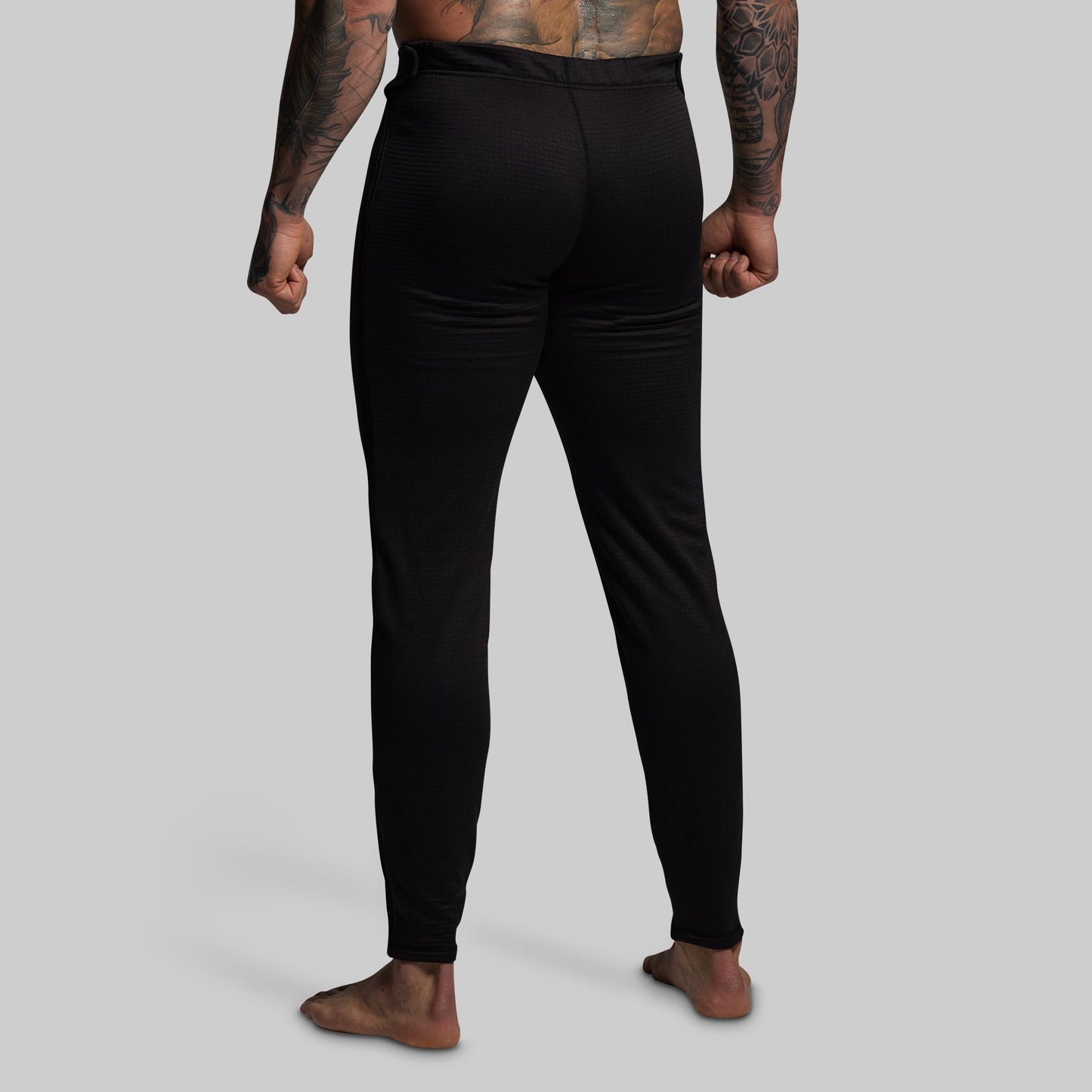 Person wearing black base layer pants on a gray background