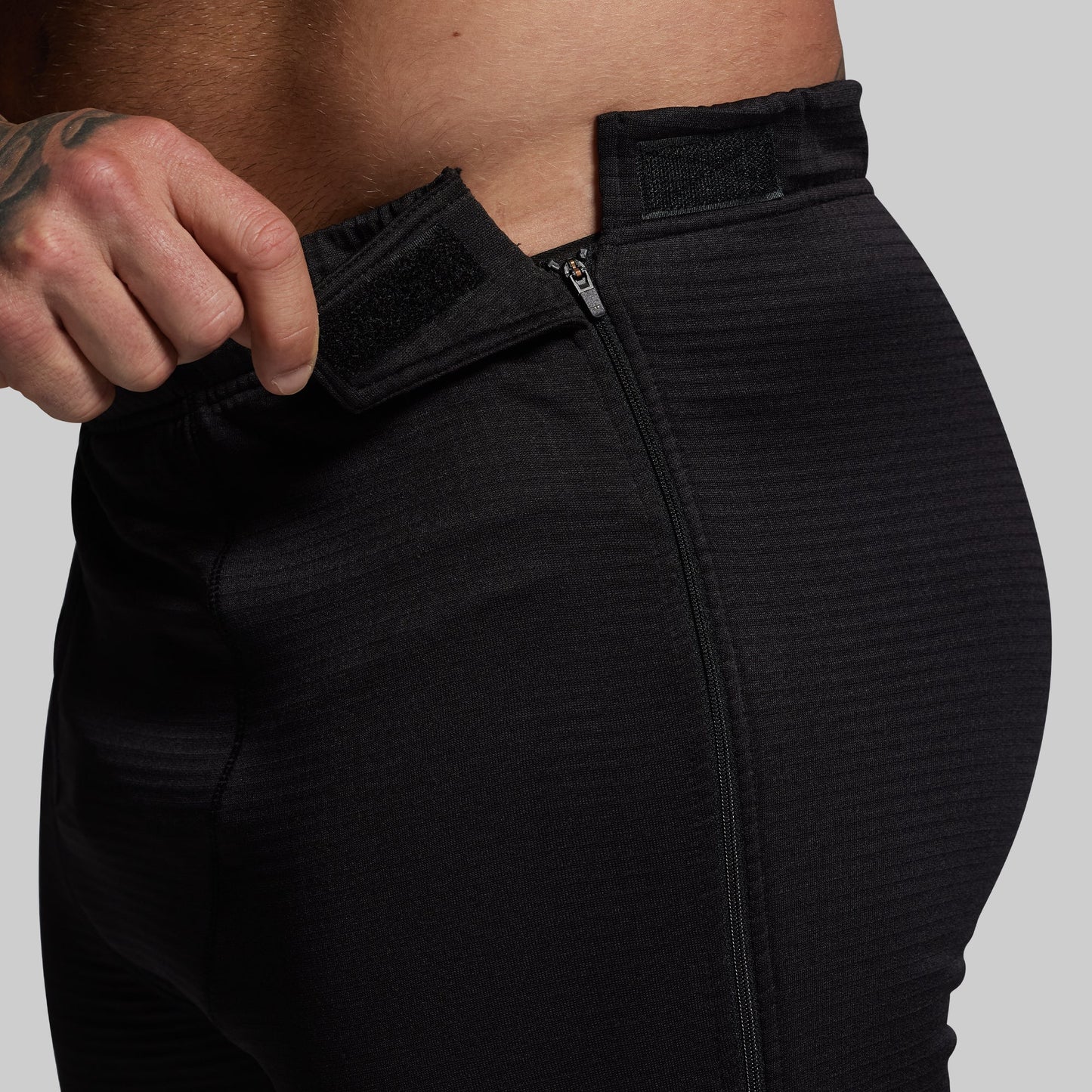 Person wearing black pants with a close-up of the zipper area on a gray background
