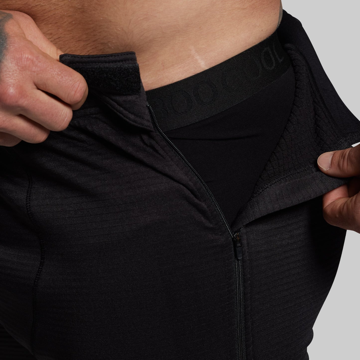Person wearing black athletic pants with a brand logo on a gray background