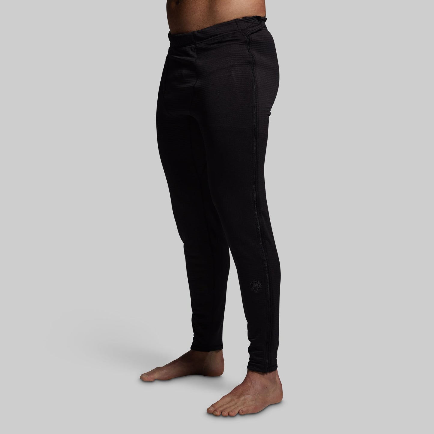 Person wearing black base layer pants on a gray background