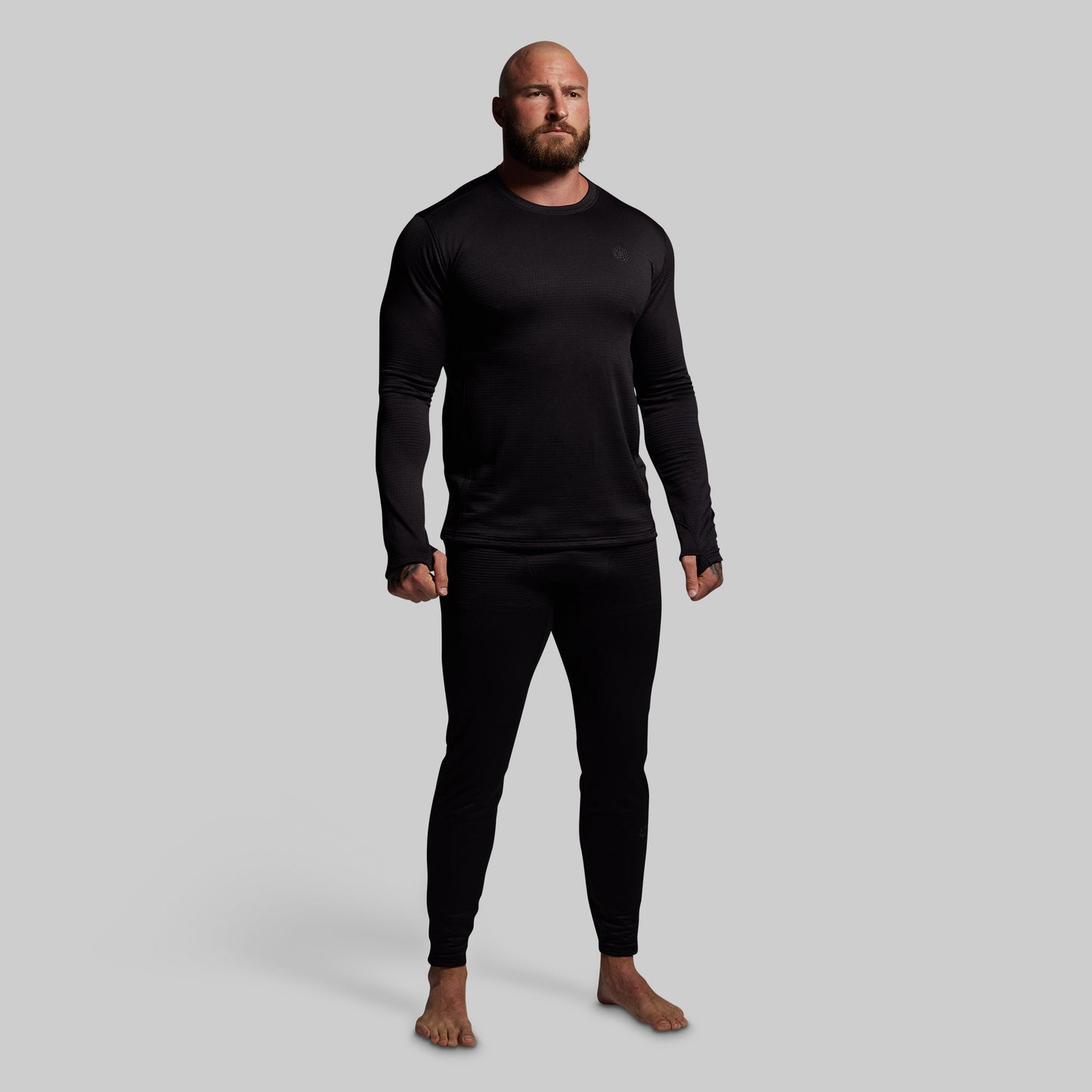 Man wearing a black long-sleeve shirt and black pants base layer set on a gray background