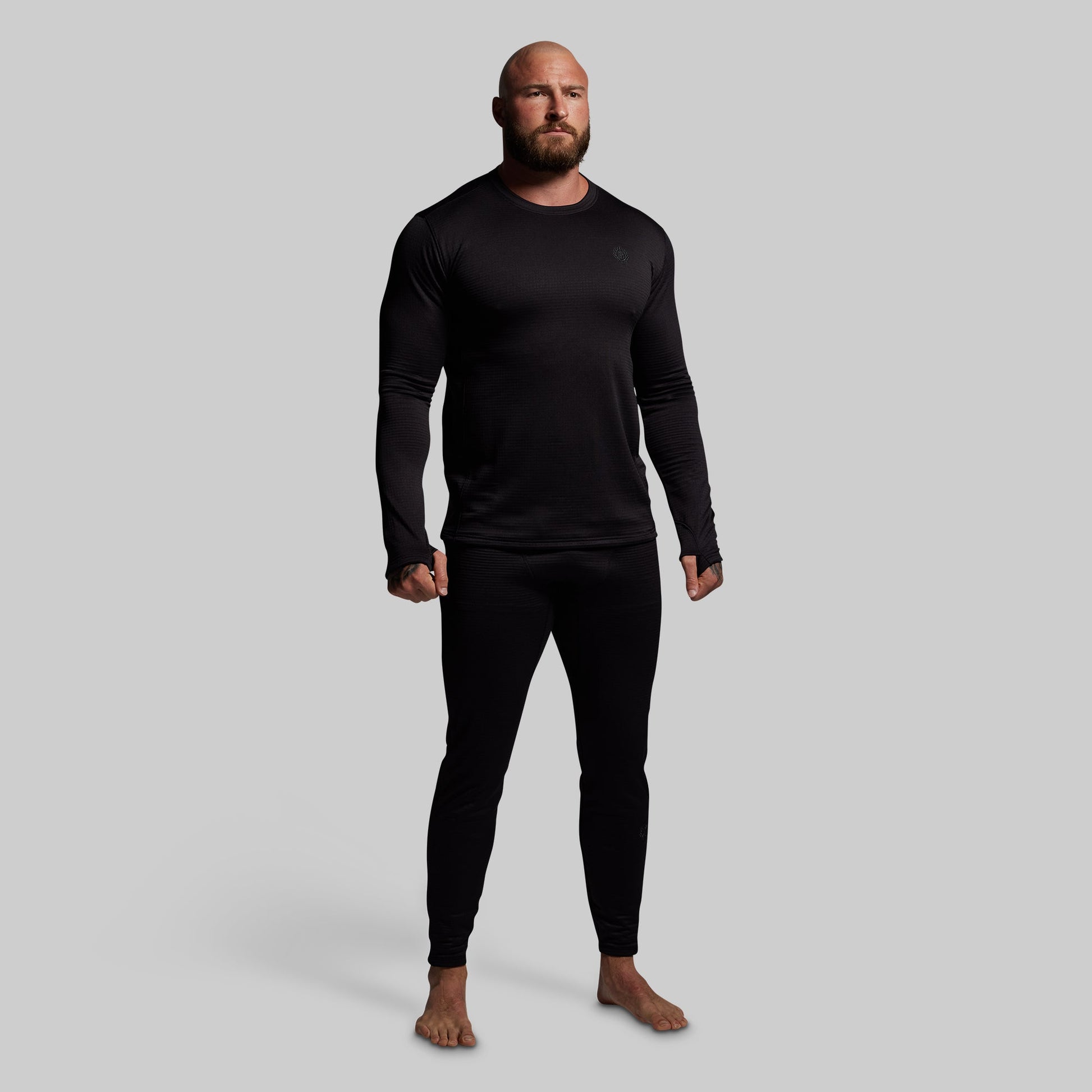 Man wearing a black long-sleeve shirt and black pants base layer set on a gray background
