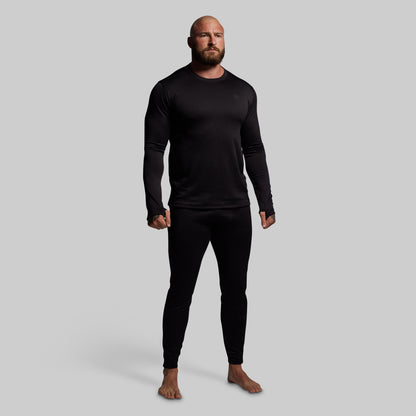 Man wearing a black long-sleeve shirt and black pants base layer set on a gray background