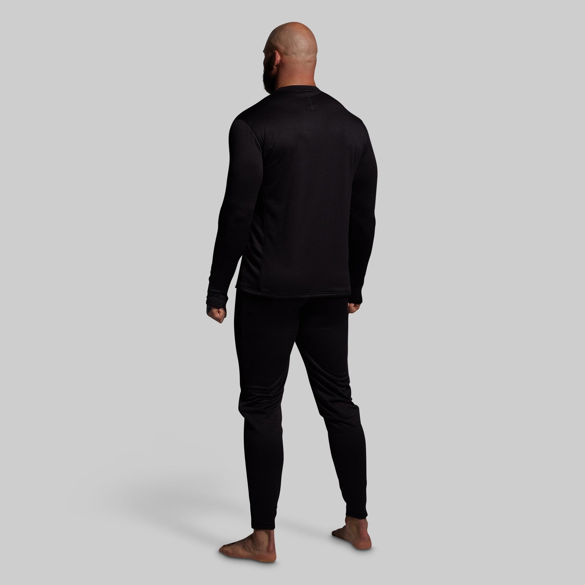 Man wearing a black long-sleeve shirt and black pants base layer set on a gray background