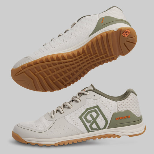 White and green athletic shoes with brown soles on a light gray background
