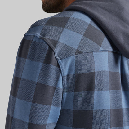Close-up of a man wearing a blue and dark gray buffalo plaid hooded shirt, showing the shoulder, collar, and hood against a light gray background.