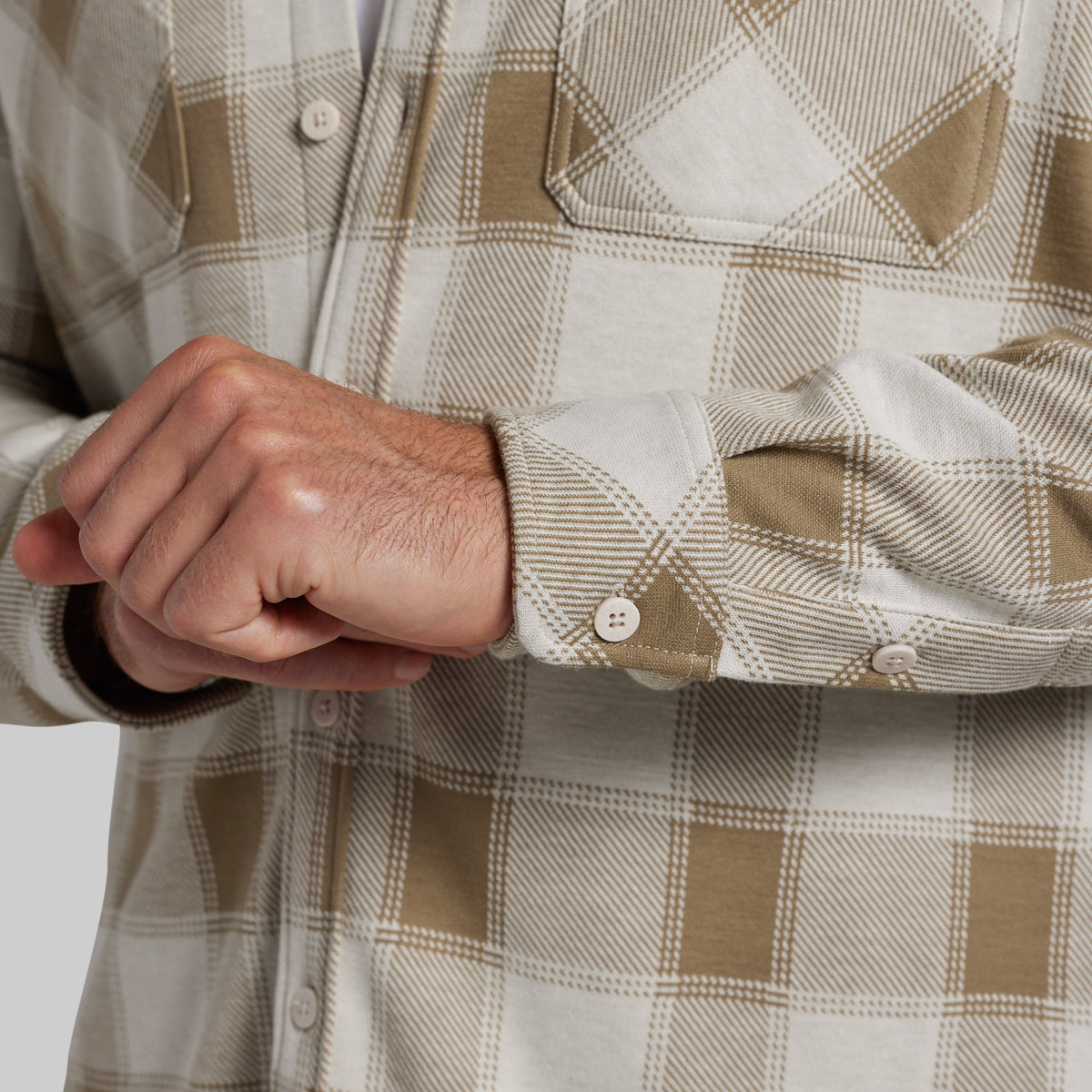 Close-up of man adjusting the cuff of a white and tan plaid flannel