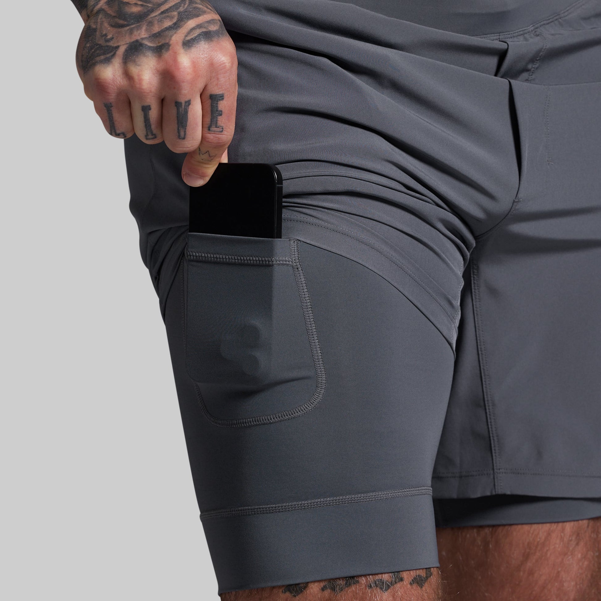 Person wearing gray shorts with a pocket, holding a phone.