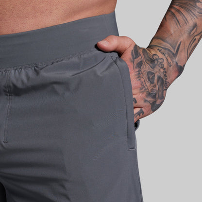 Person wearing gray shorts with a tattooed arm on a light gray background