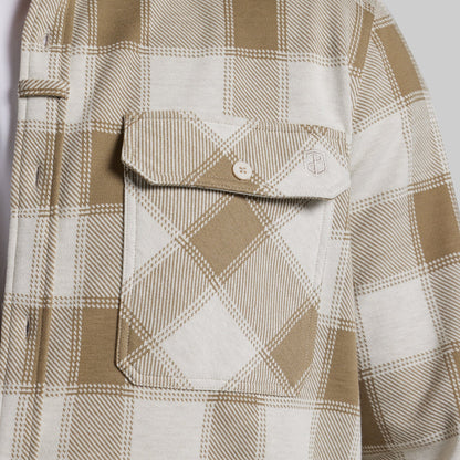Close-up of a plaid button-up shirt with a chest pocket, featuring a tan and off-white check pattern.
