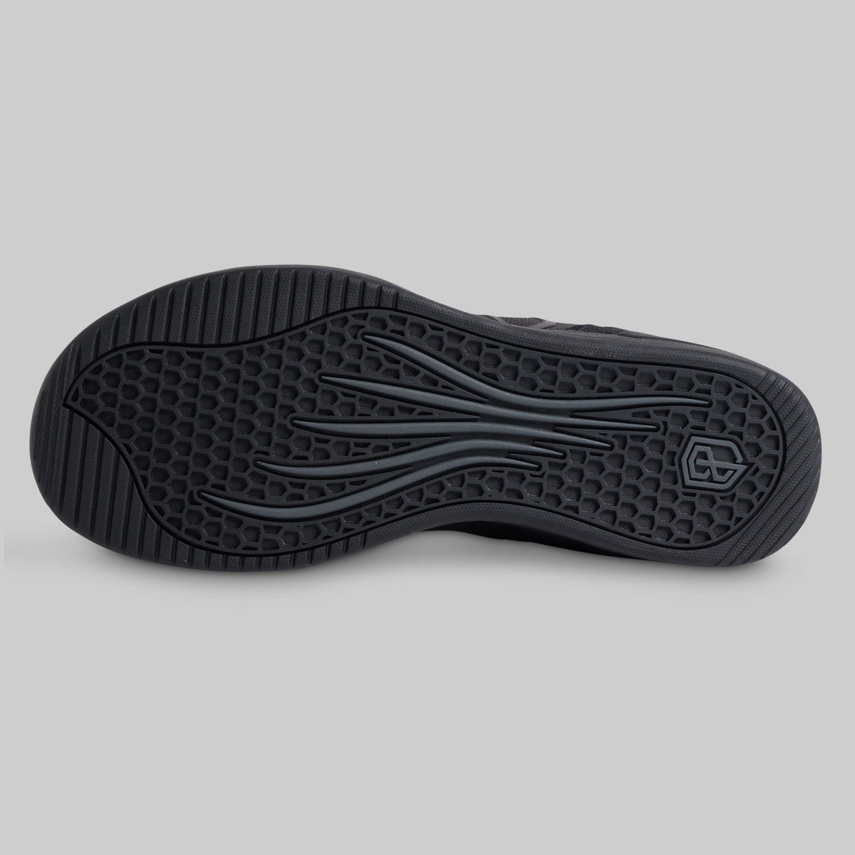 The black rubber outsole of a shoe, showing a textured honeycomb pattern and wavy tread design, photographed from a top-down view on a neutral gray background.