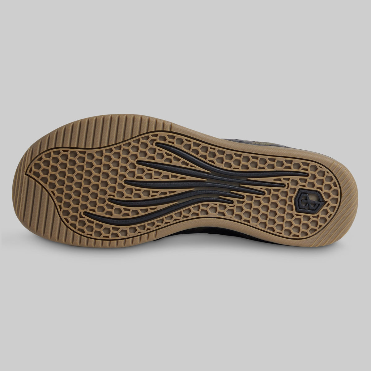 The outsole of a shoe shown from a top-down view, featuring a tan rubber base with a black honeycomb pattern and stylized black tread details, set against a solid gray background.