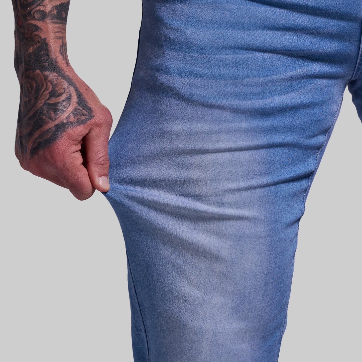 Close-up of a person wearing blue jeans with a tattooed hand on a gray background