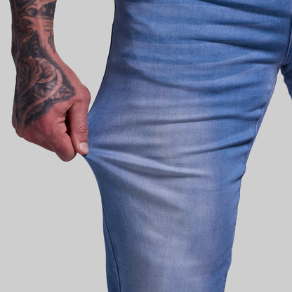Close-up of a person wearing blue jeans with a tattooed hand on a gray background
