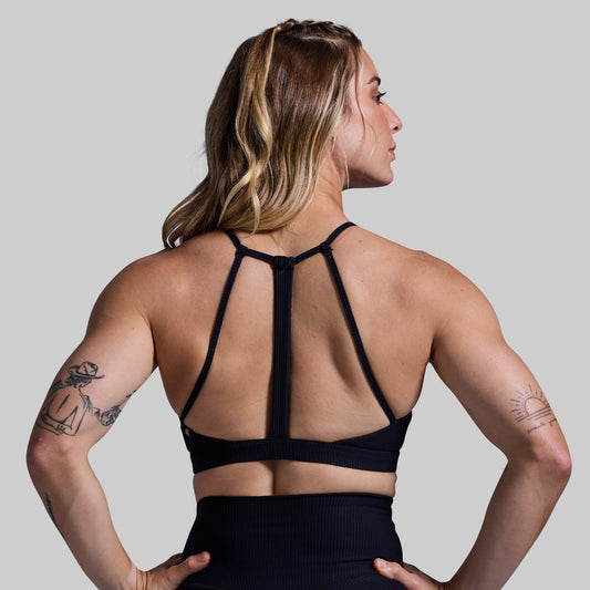 Woman wearing a black sports bra with thin straps on a plain background