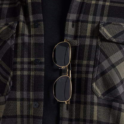 Sunglasses hanging from the placket of a black and gray plaid flannel shirt.