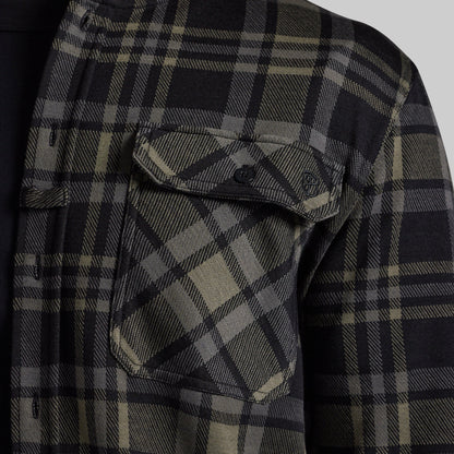 Close-up of a black and greu plaid flannel shirt, showing a chest pocket with a button flap and a small shield logo patch.