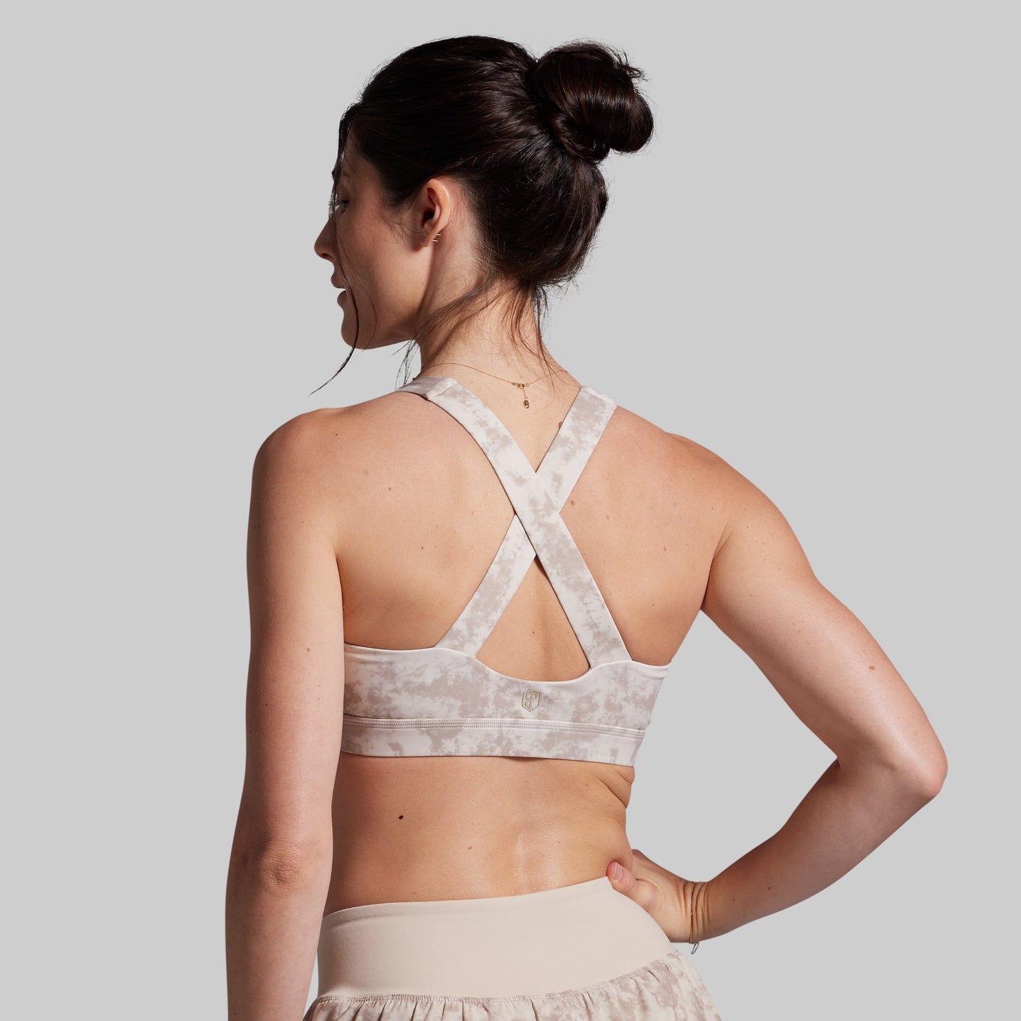 Woman wearing a light-colored sports bra and shorts on a plain background